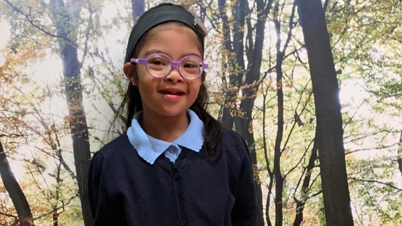 Child with Down syndrome poses in school uniform in front of some trees