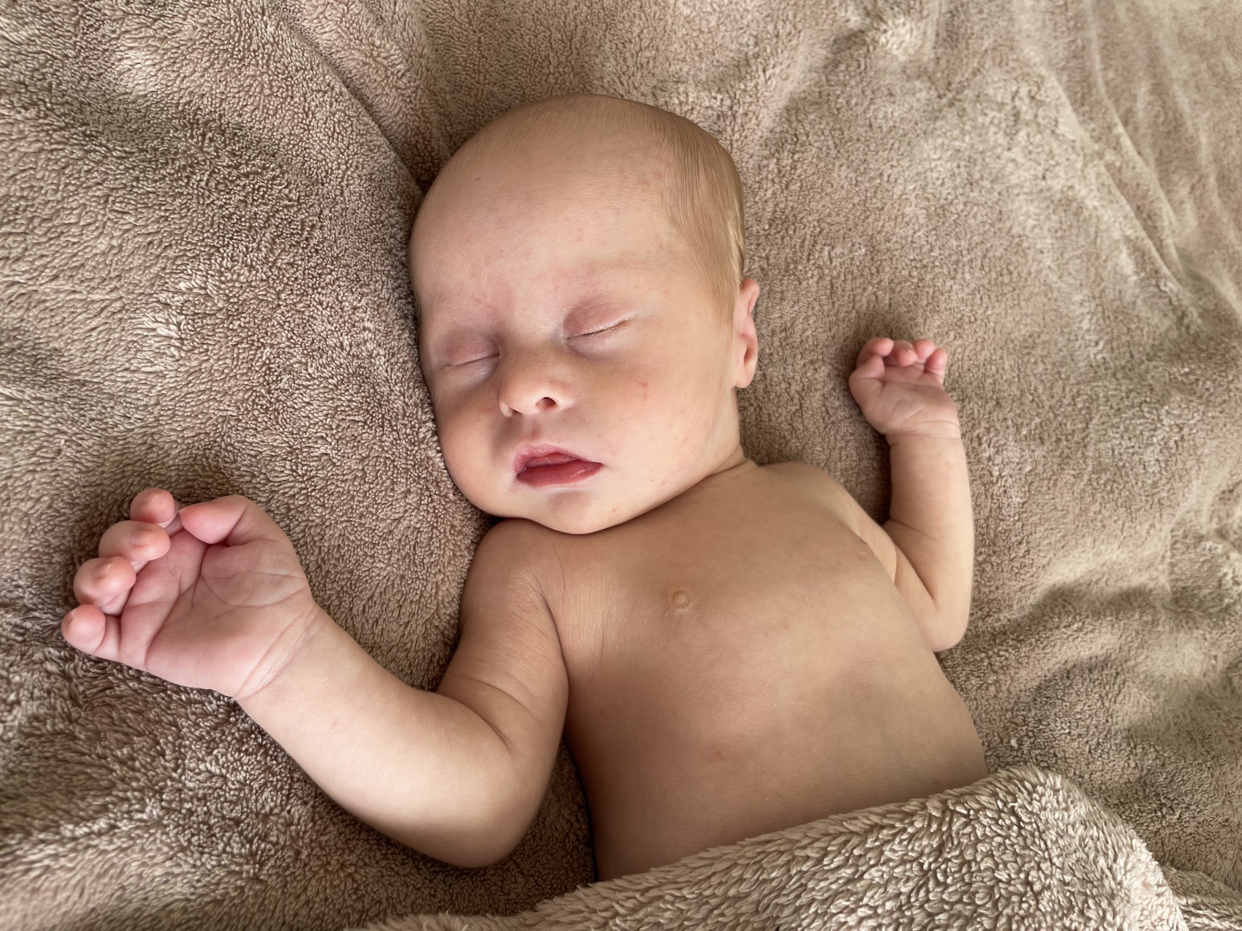 baby lying on a soft blanket with its eyes closes and arms splayed out