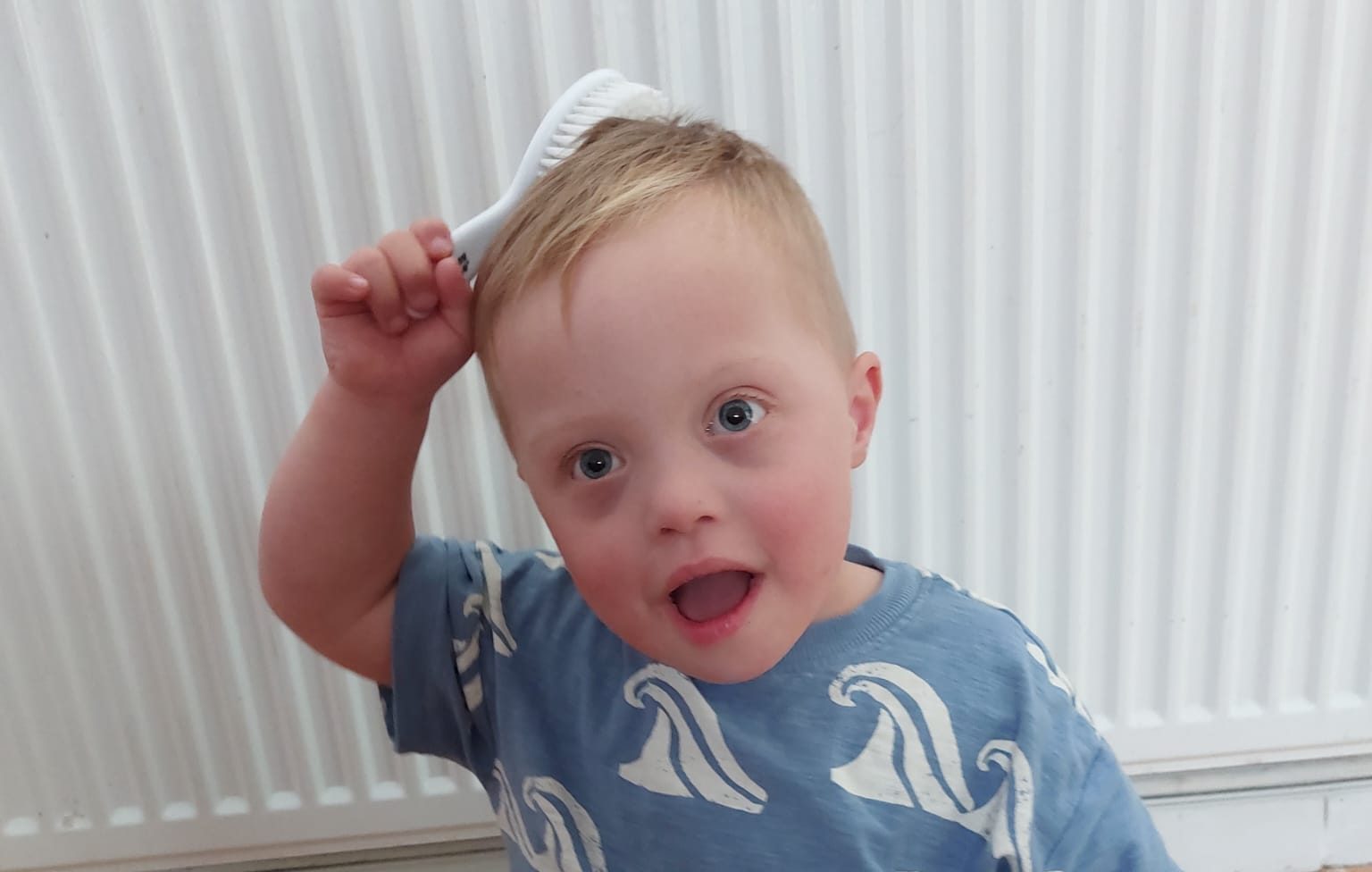 Child with down syndrome is holding a hairbrush onto their head and brushing their hair