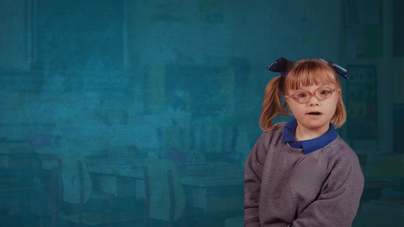 Child with down syndrome in primary school uniform posing for her school pic. shes wearing pig tails with a cute bow on each one and she has a fringe and pink glasses