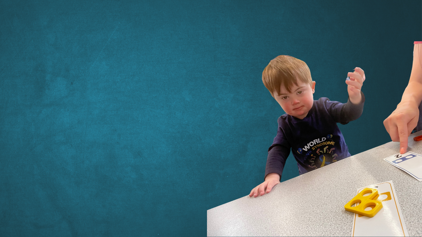 Parker at nursery with a table and numicon pieces in front of him teaching him numbers