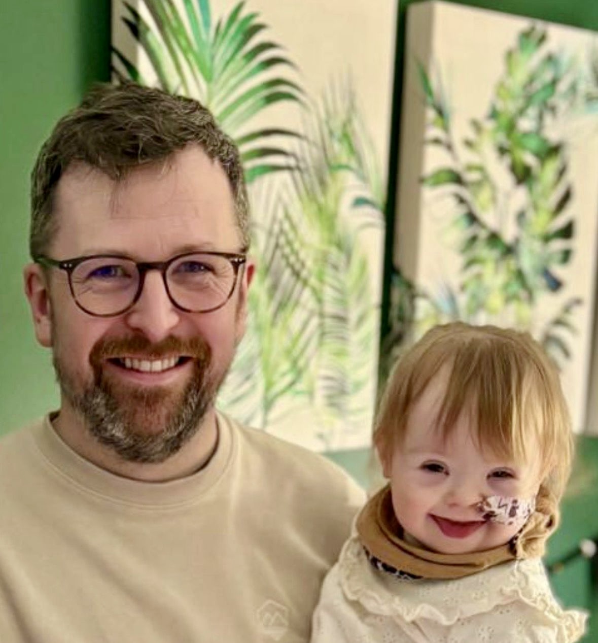 David is posing with Norah in this photograph. Norah has an infectious grin and is wearing a scarf. She also has an NG tube