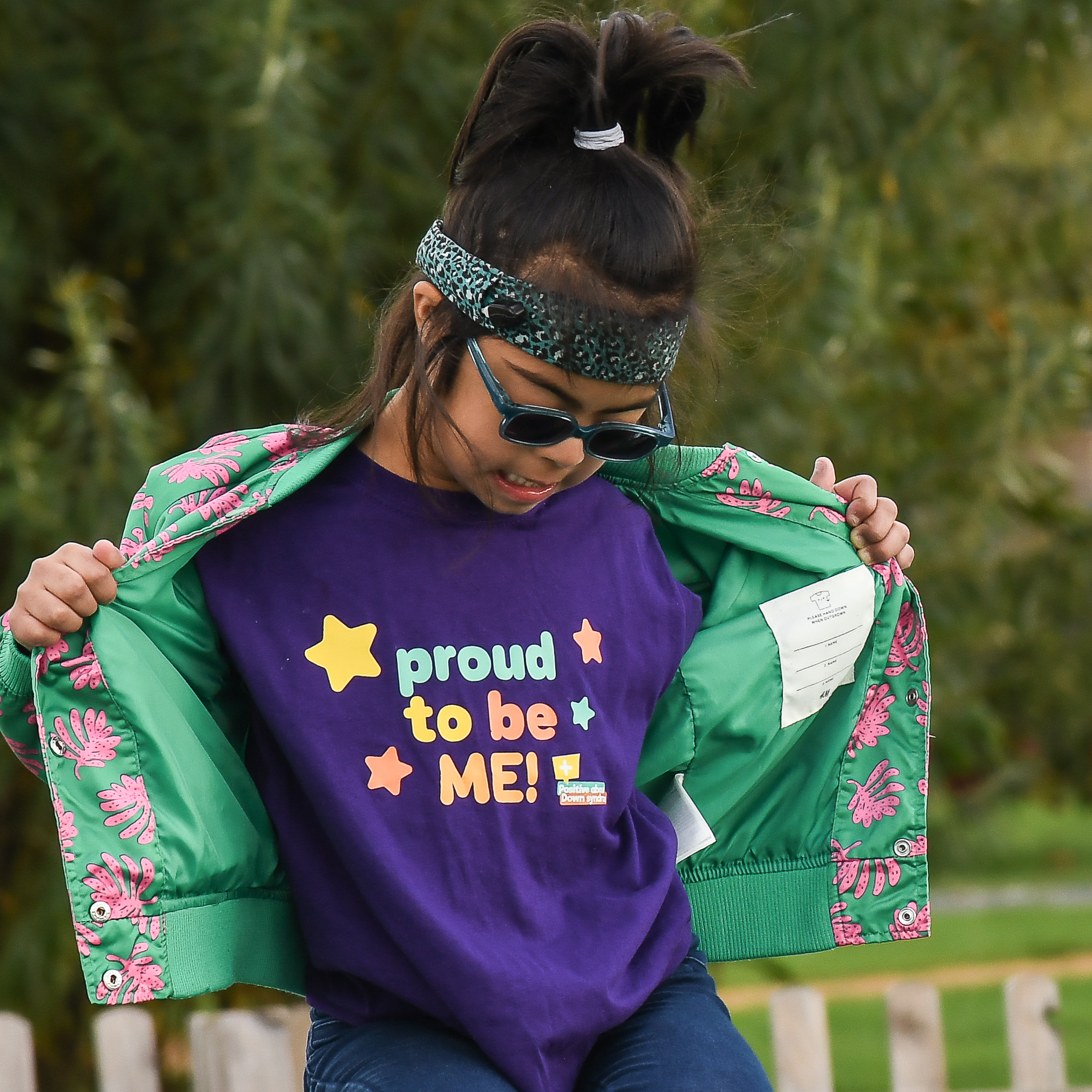 Child with down syndrome is opening her coat out and looking towards her 'proud to be me' shirt