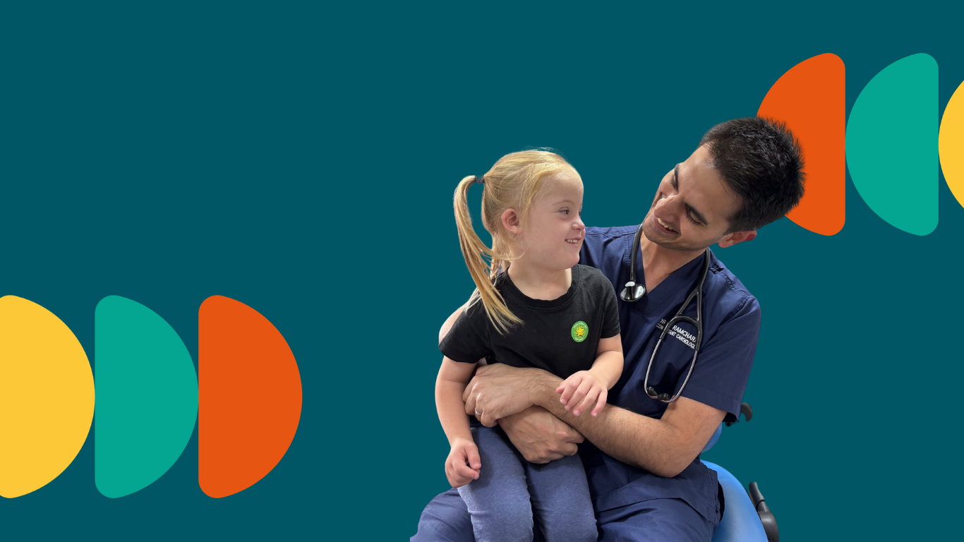 young girl with down syndrome sits on the lap of a medical professional who has a stethoscope around his neck